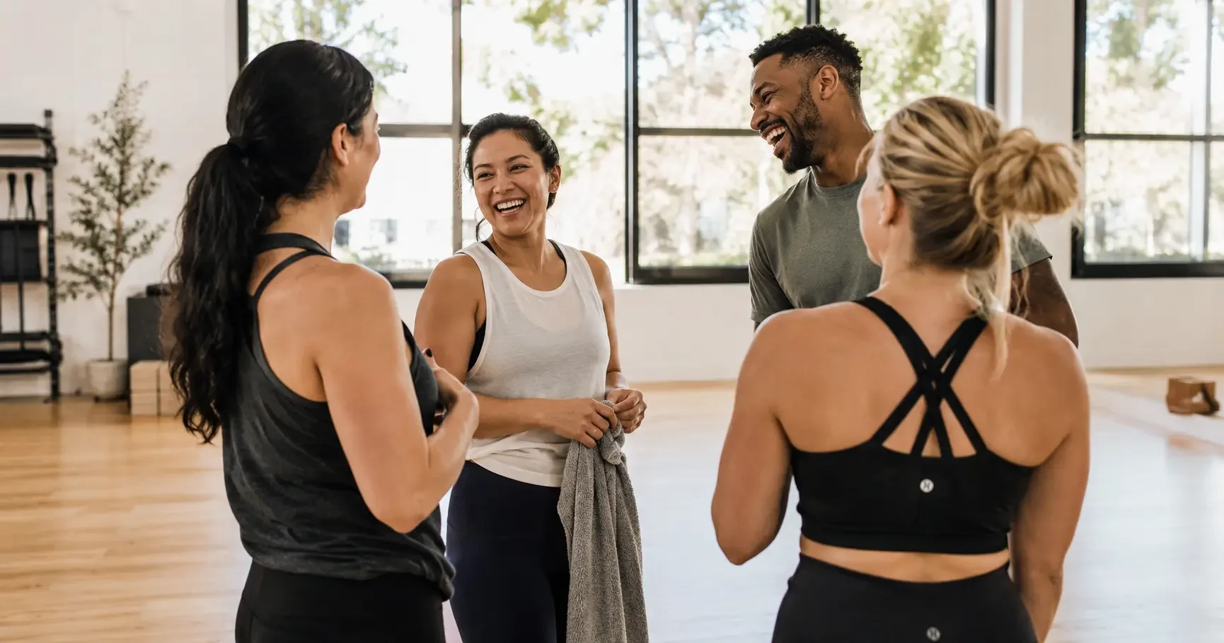 Small group of wellness studio members after a class in natural conversation, genuine warmth and community feeling, bright studio with natural light, editorial documentary portrait