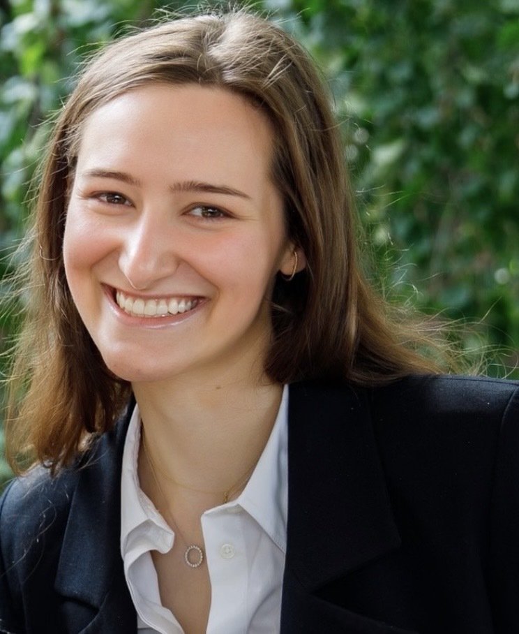 A white woman with brown, shoulder-length hair, wearing a navy suit jacket and white collared shirt.