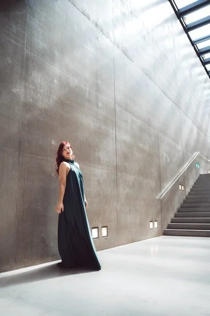 Founder in a long gown in a concrete stairwell, brand photography by Tanja Pleis