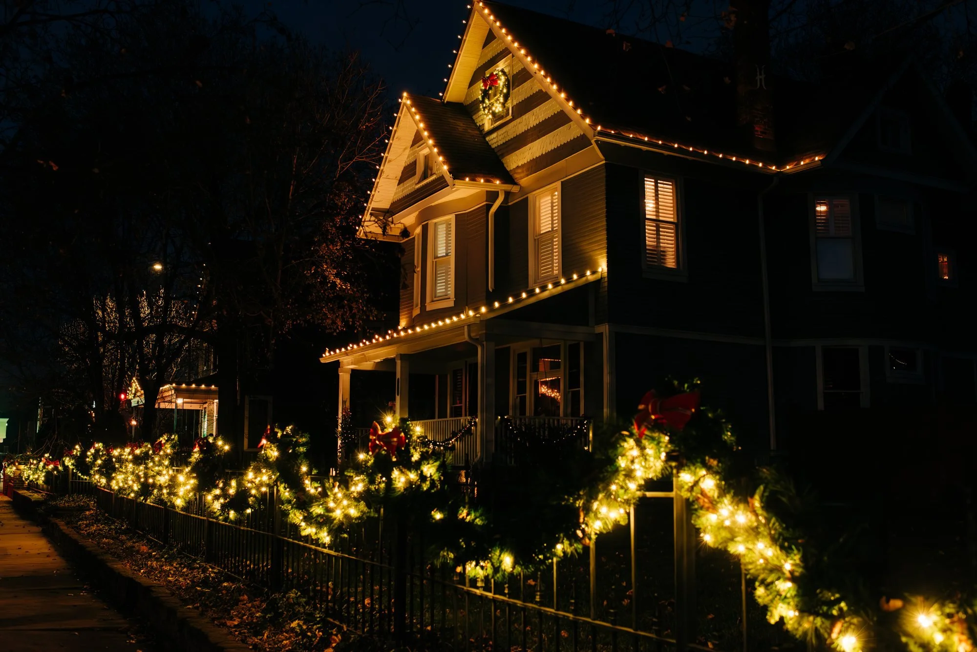 Lightin' Up installation with warm white roofline lights and illuminated garland along the front fence