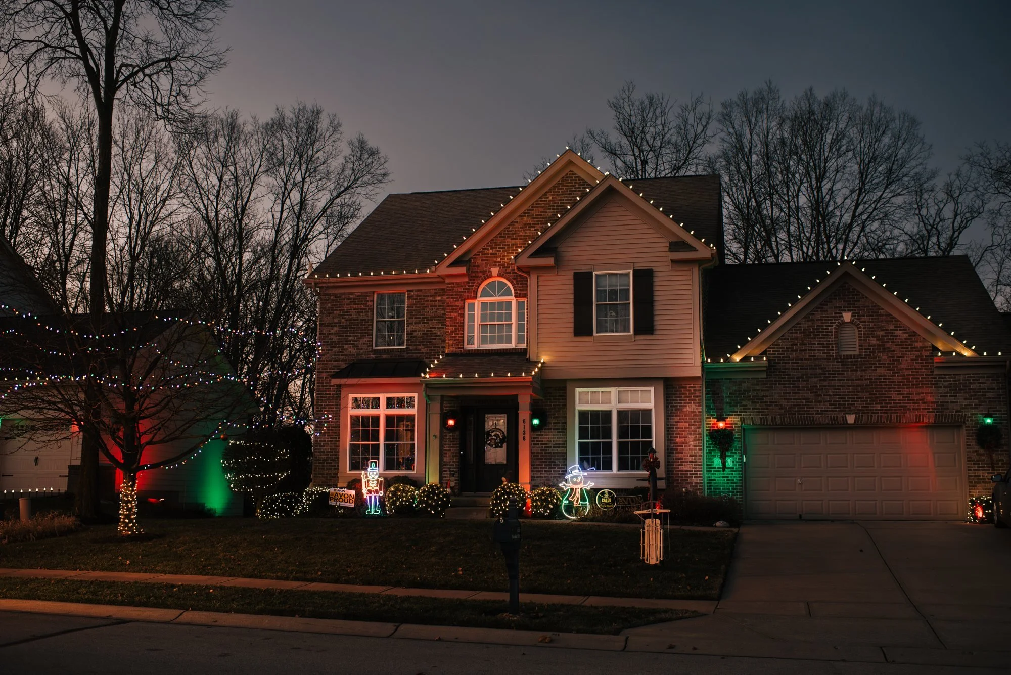 Two-story home with warm white roofline lighting and red and green landscape accents
