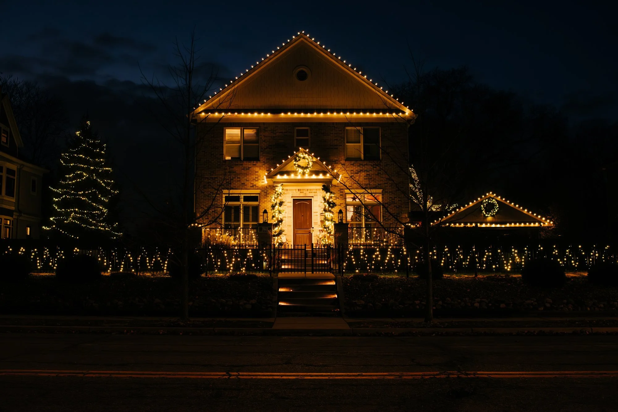 Traditional home with warm white roofline lights and illuminated garland around its entrance