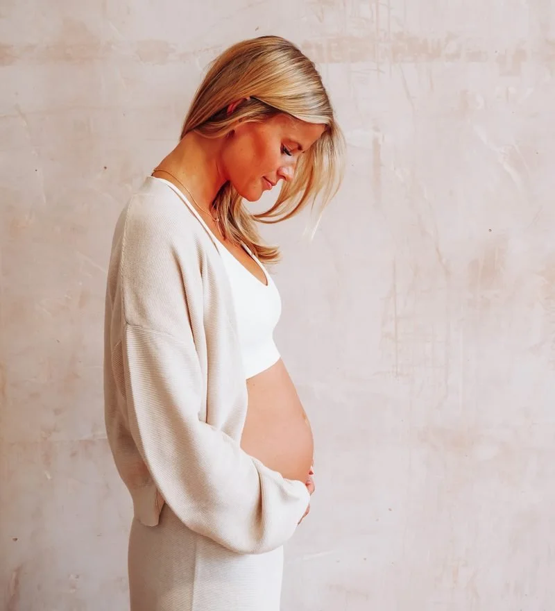 Pregnant woman in soft knitwear looking down at her bump