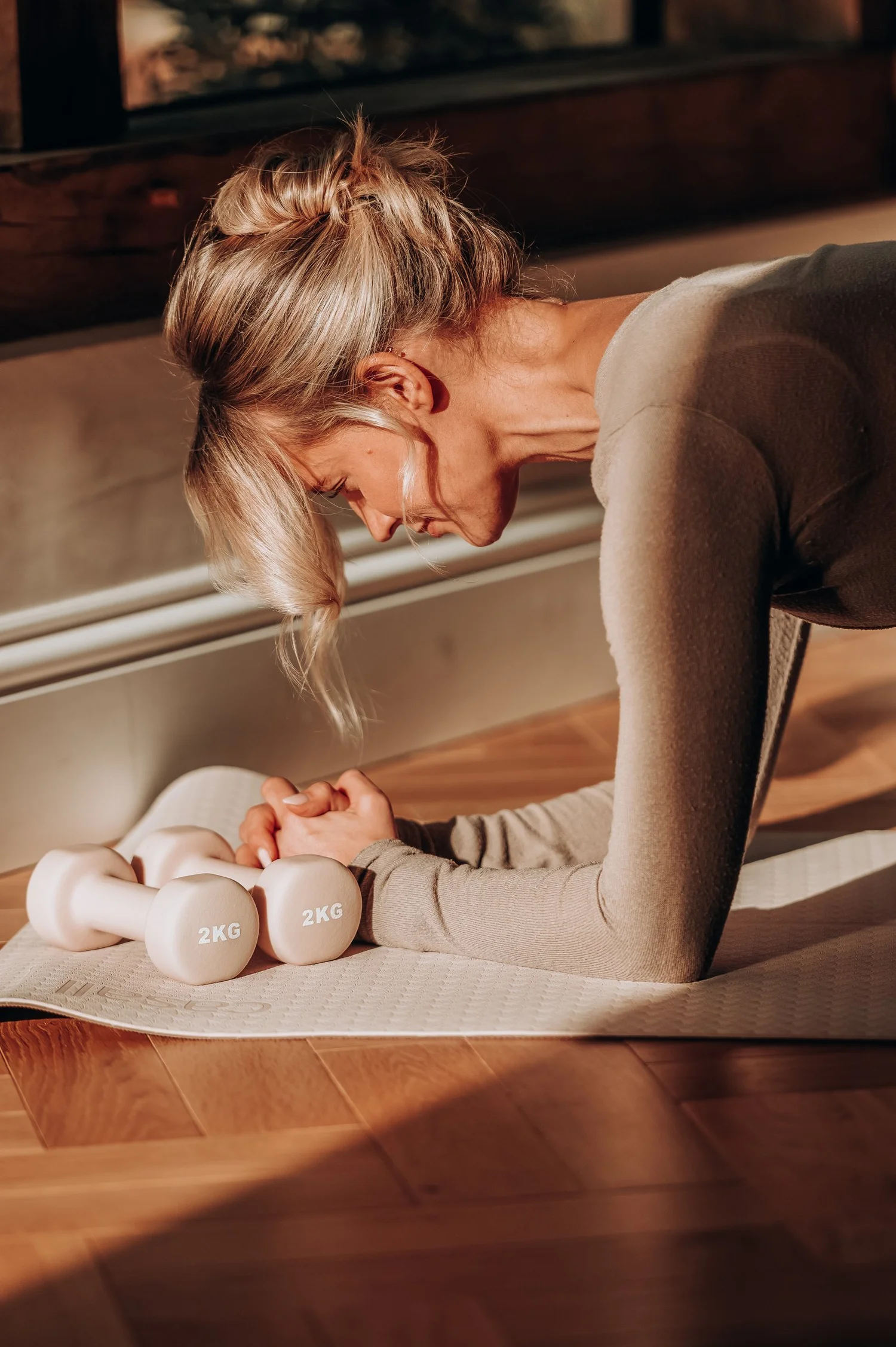 Gen holding a forearm plank on a mat beside two 2kg dumbbells