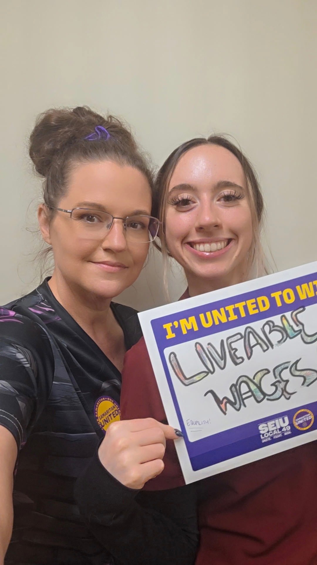 Two members smile with an “I’m united to win” sign that reads “Livable wages.”