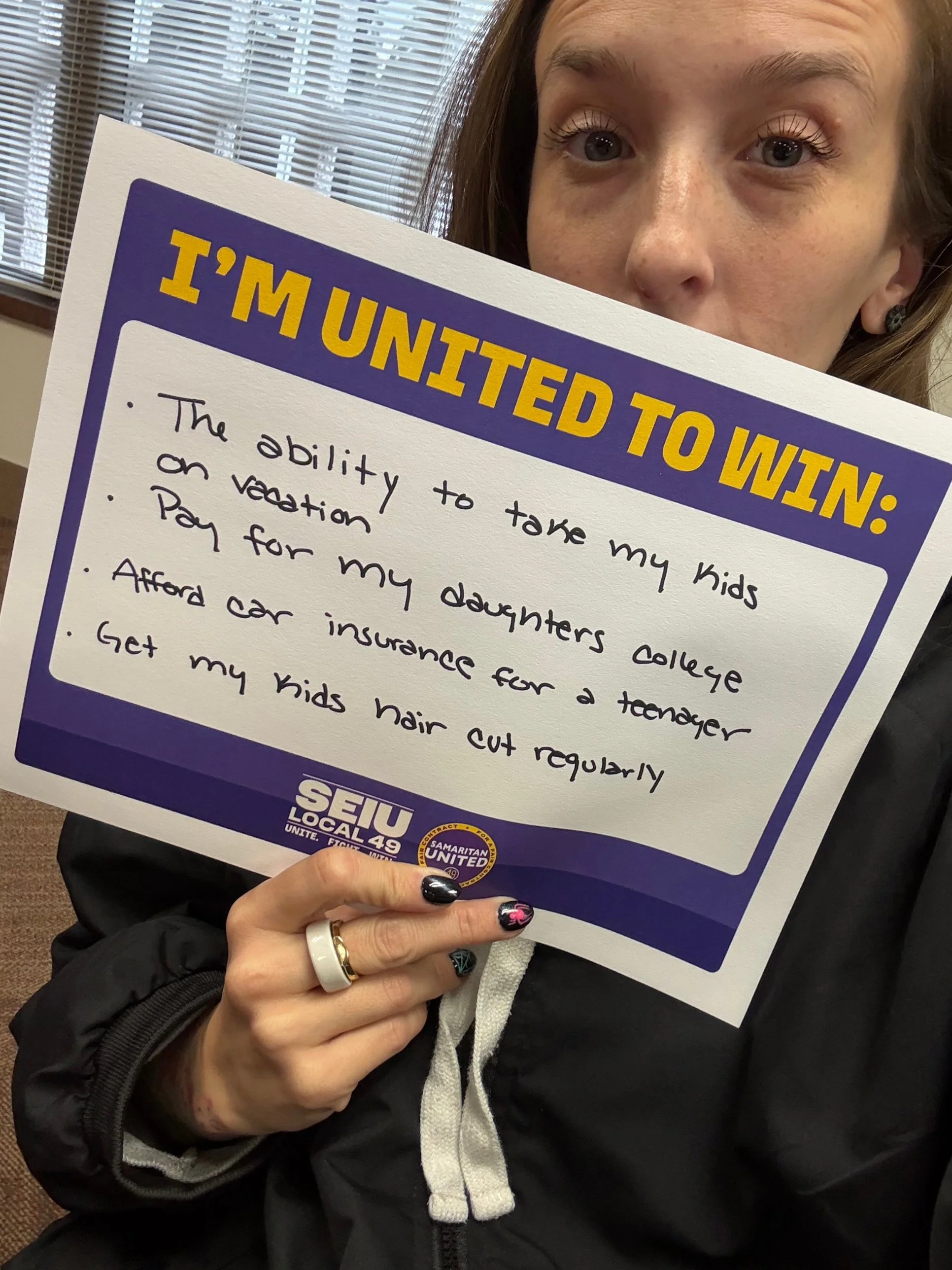A member holds a sign that reads: “I’m united to win: The ability to take my kids on vacation, pay for my daughter’s college, afford car insurance for a teenager, get my kids’ hair cut regularly.”