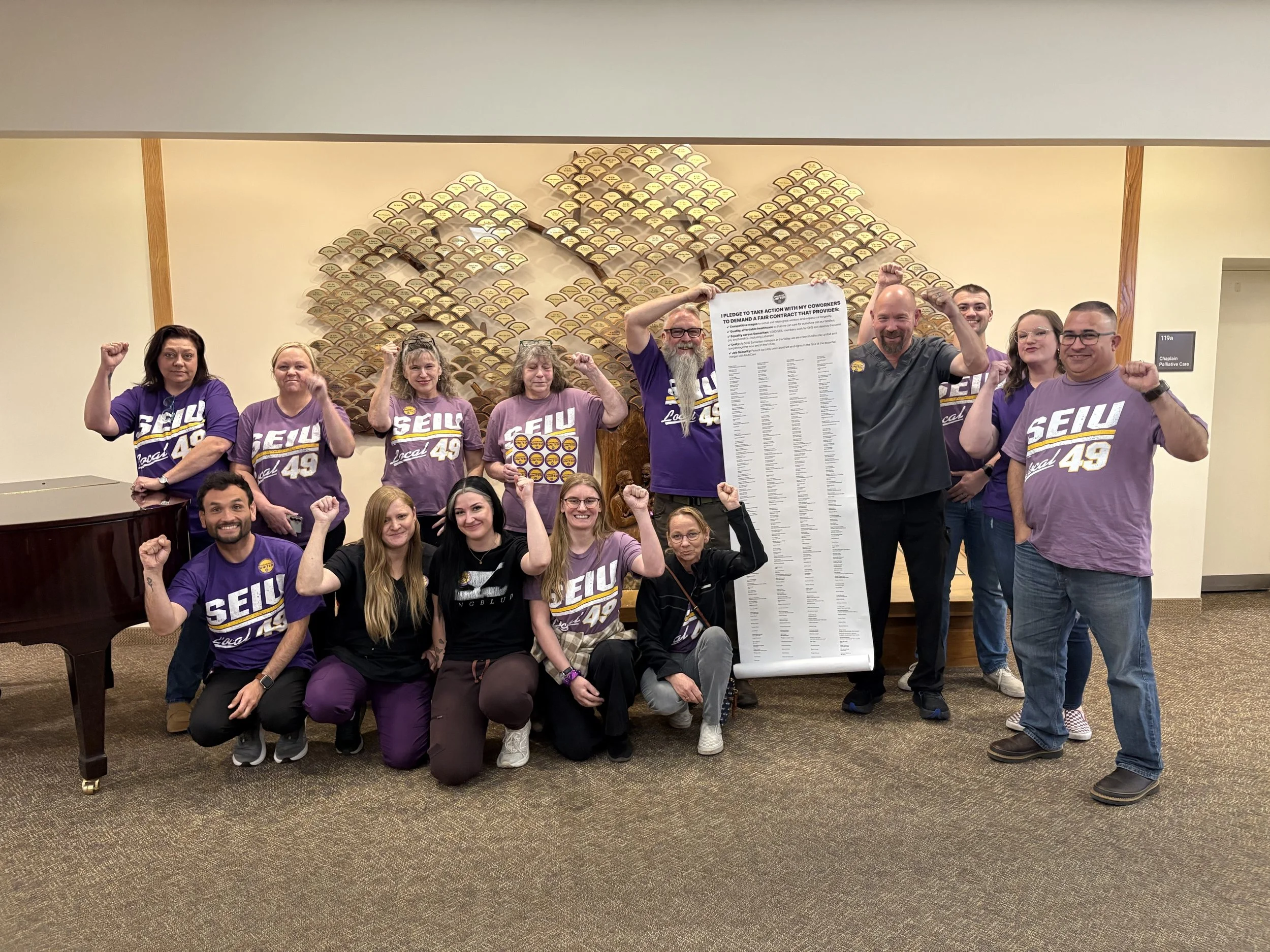 Samaritan Lebanon caregivers in purple SEIU 49 shirts raise their fists beside a long scroll of petition signatures.