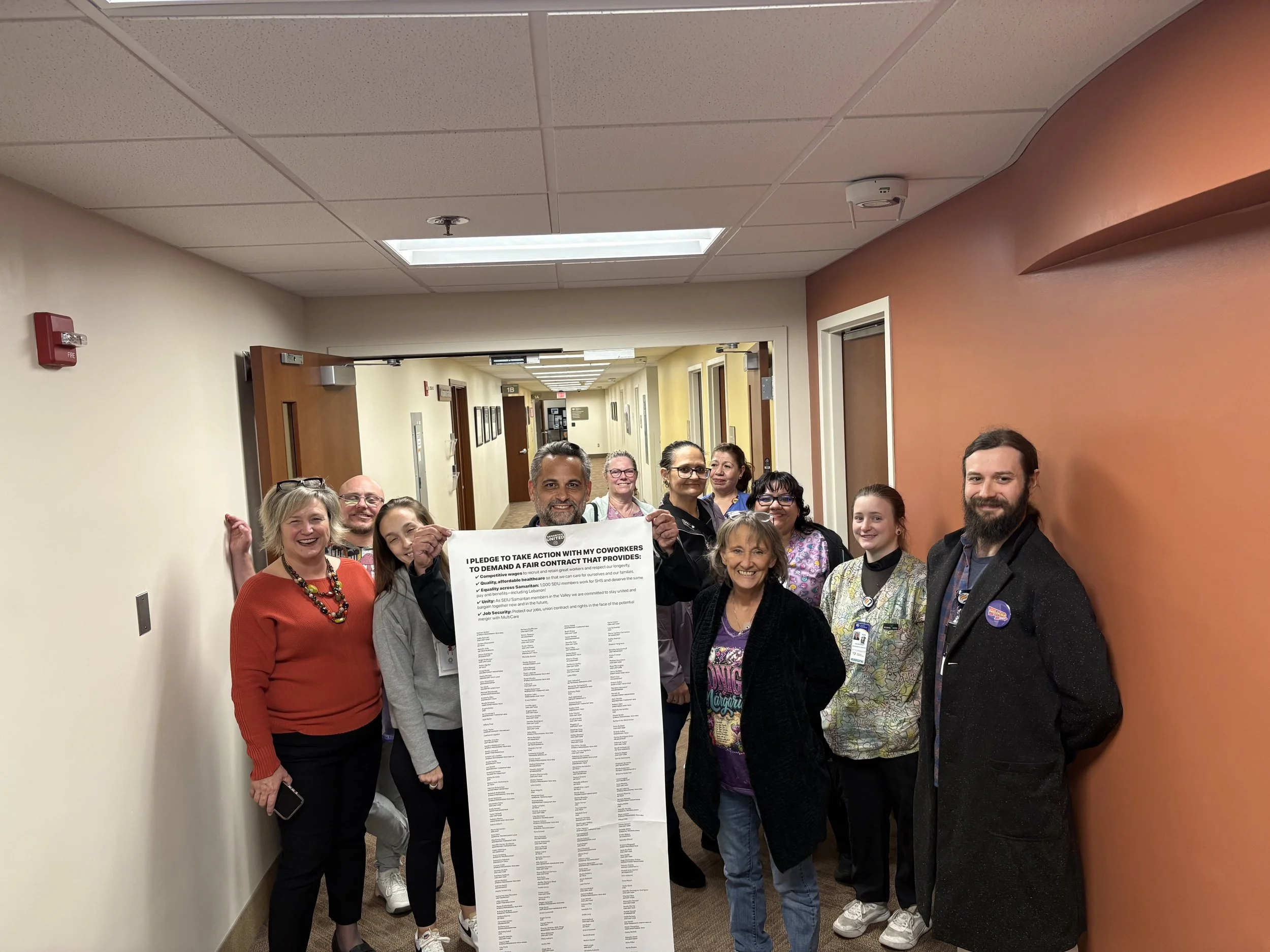 Albany General Hospital caregivers stand in a hallway holding up a long scroll of petition signatures.