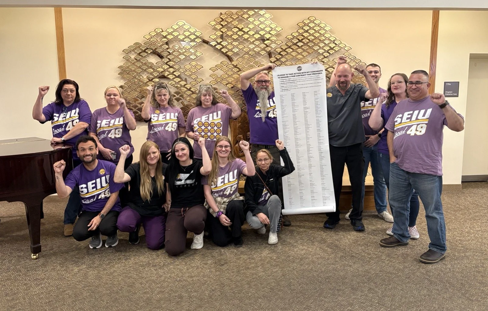 Samaritan Lebanon caregivers in purple SEIU 49 shirts raise their fists beside a long scroll of bargaining priorities petition signatures.