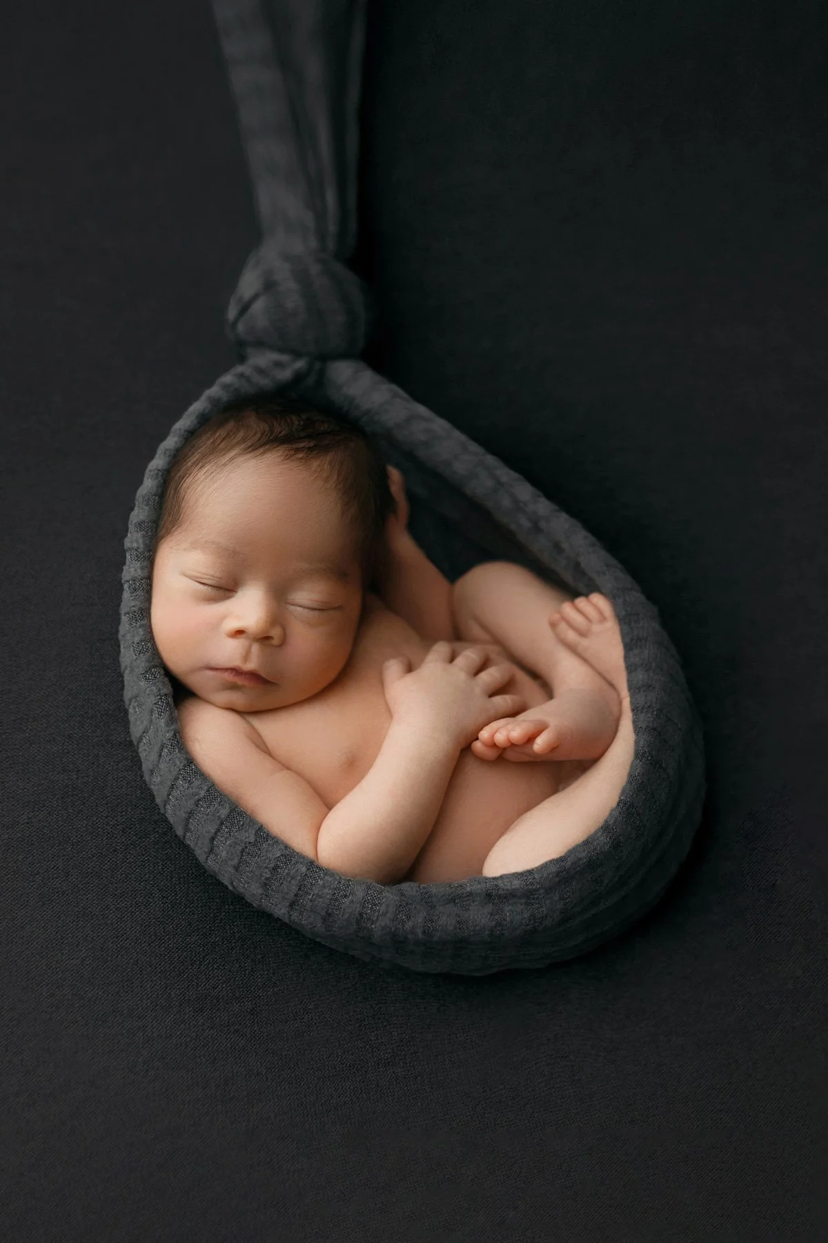 Newborn baby posed dark gray knit wrap stork pose