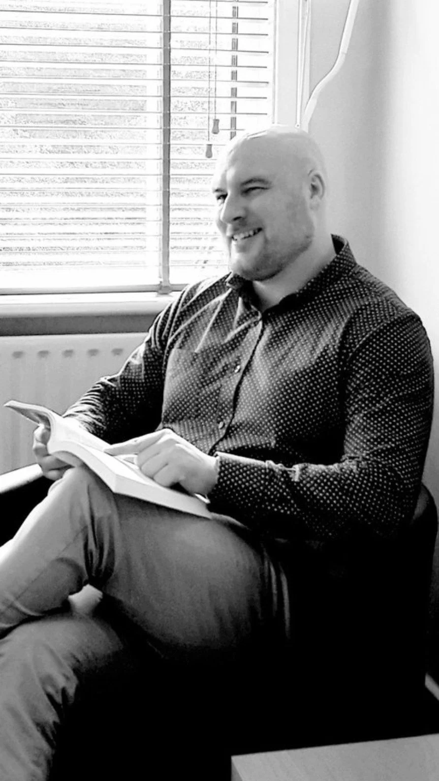 Dr Colm Marren seated and smiling, holding a notebook.