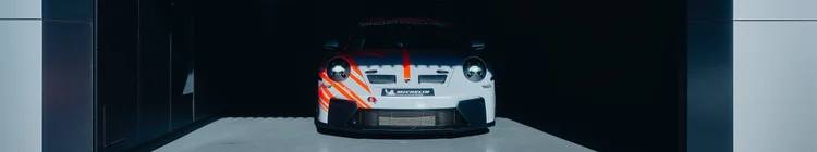 Front view of a white Porsche race car with red accents in a shadowed garage, with the complete car visible