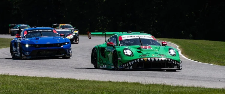 Green Porsche race car leading a blue Ford Mustang and other cars on a circuit.