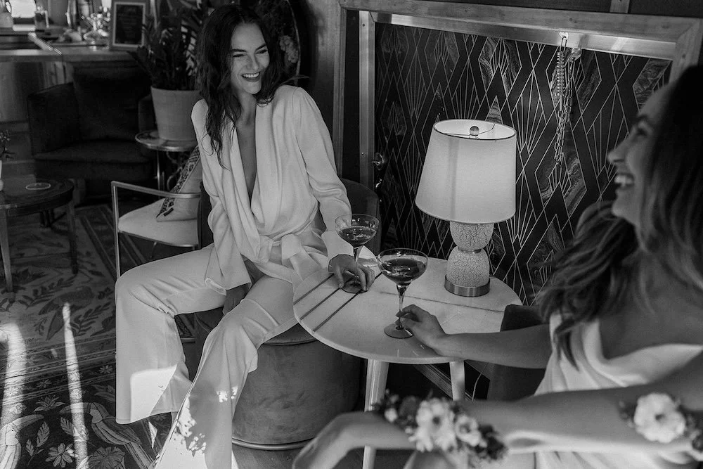 Two women laughing over cocktails at a small side table inside the Stargazer Social Club suite.