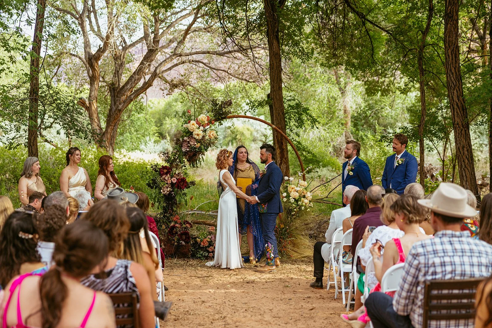 Outdoor ceremony arch decorated with maroon fabric and florals in a natural setting