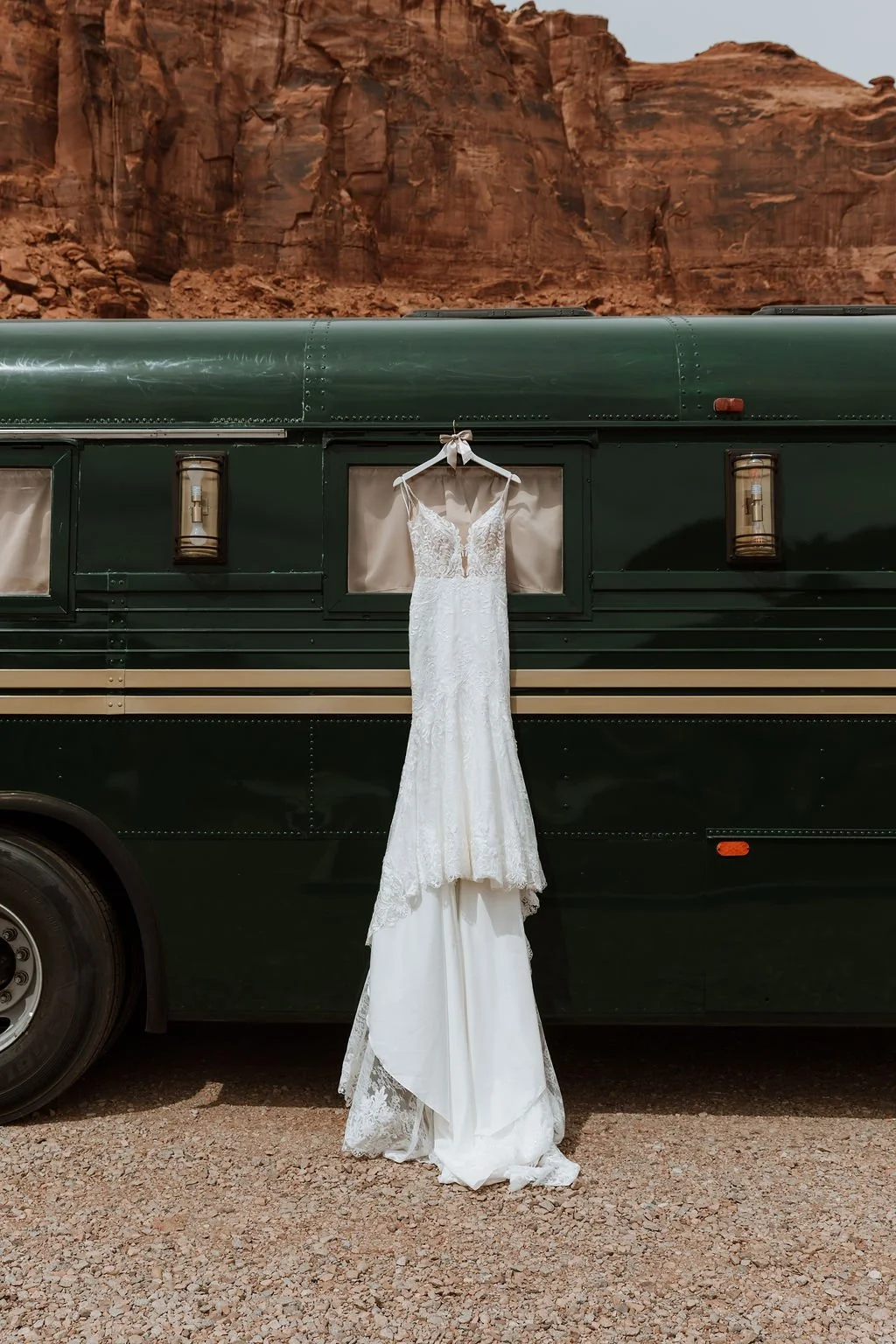 A lace wedding gown hanging on the exterior of the Stargazer bus with towering red rock cliffs in the background.