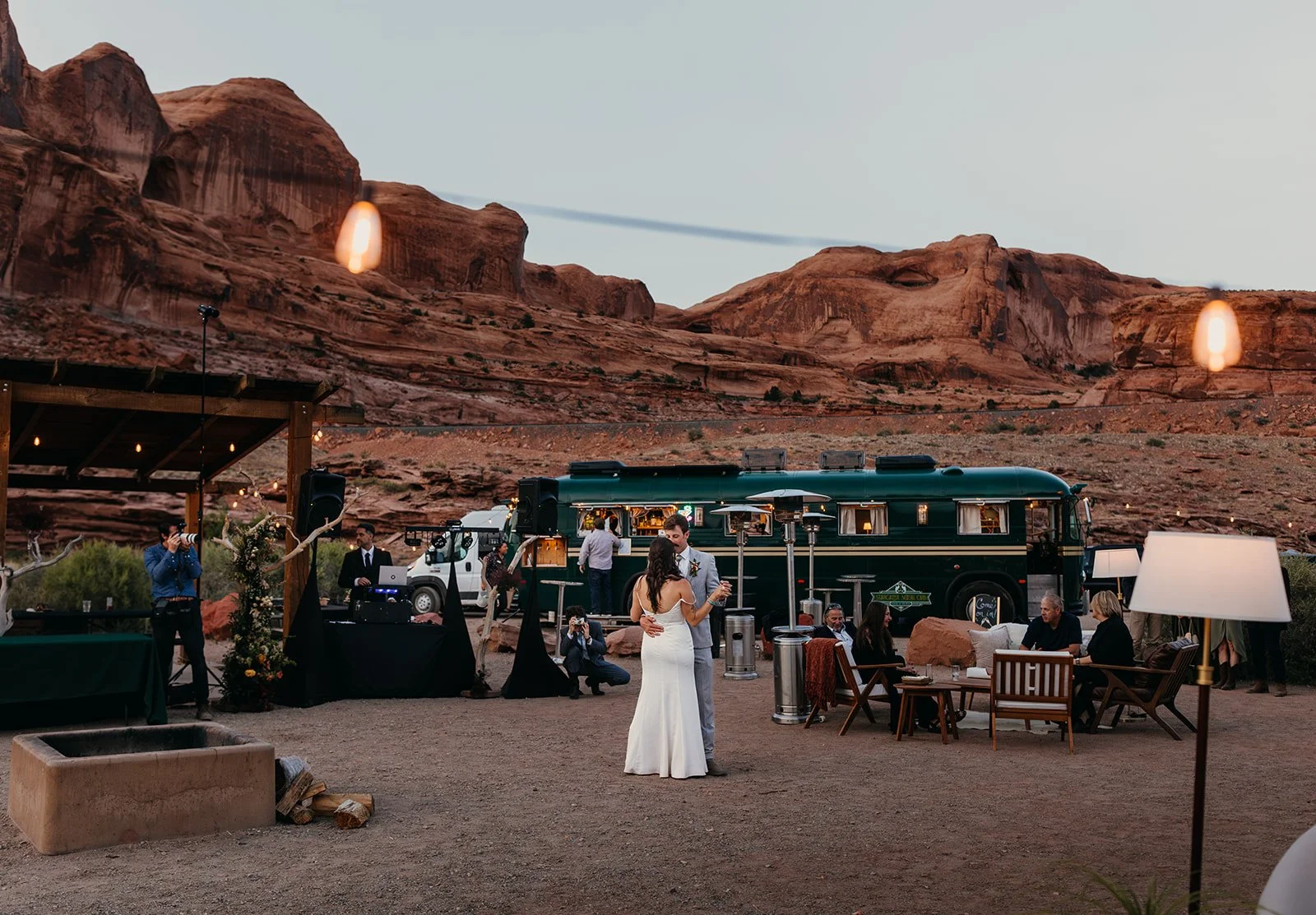 Outdoor desert wedding setup with string lights and the vintage Stargazer bus.