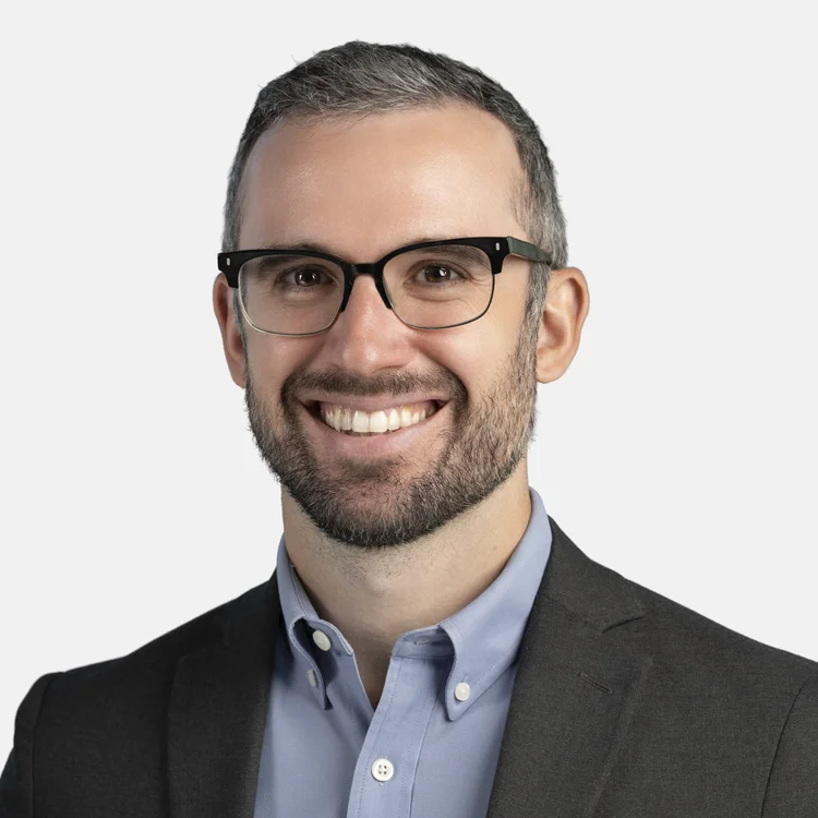 Smiling man in dark glasses and a blazer against a light background