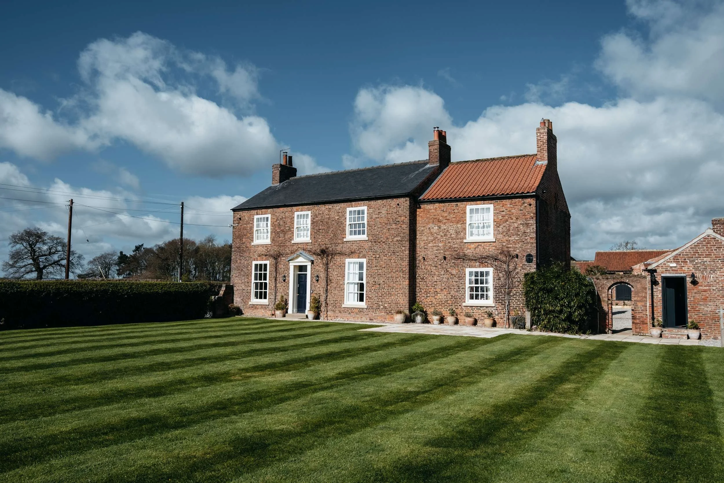Farmhouse and striped lawn under blue sky at Thirsk Lodge Barns wedding venue in North Yorkshire