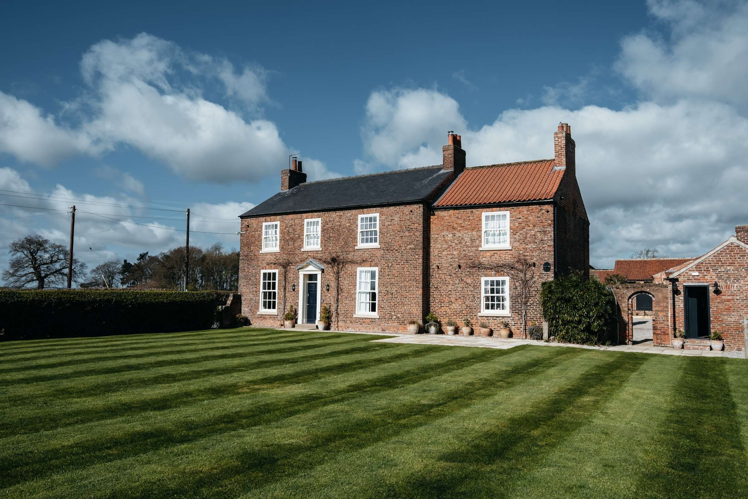 Farmhouse and striped lawn under blue sky at Thirsk Lodge Barns wedding venue in North Yorkshire