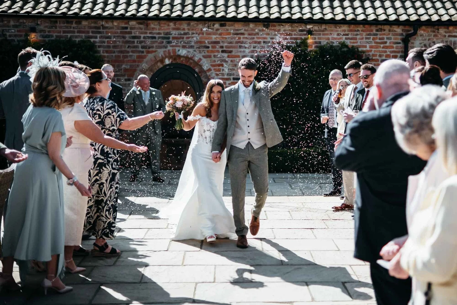 Confetti thrown over the couple in the courtyard at Thirsk Lodge Barns, barn roofline behind