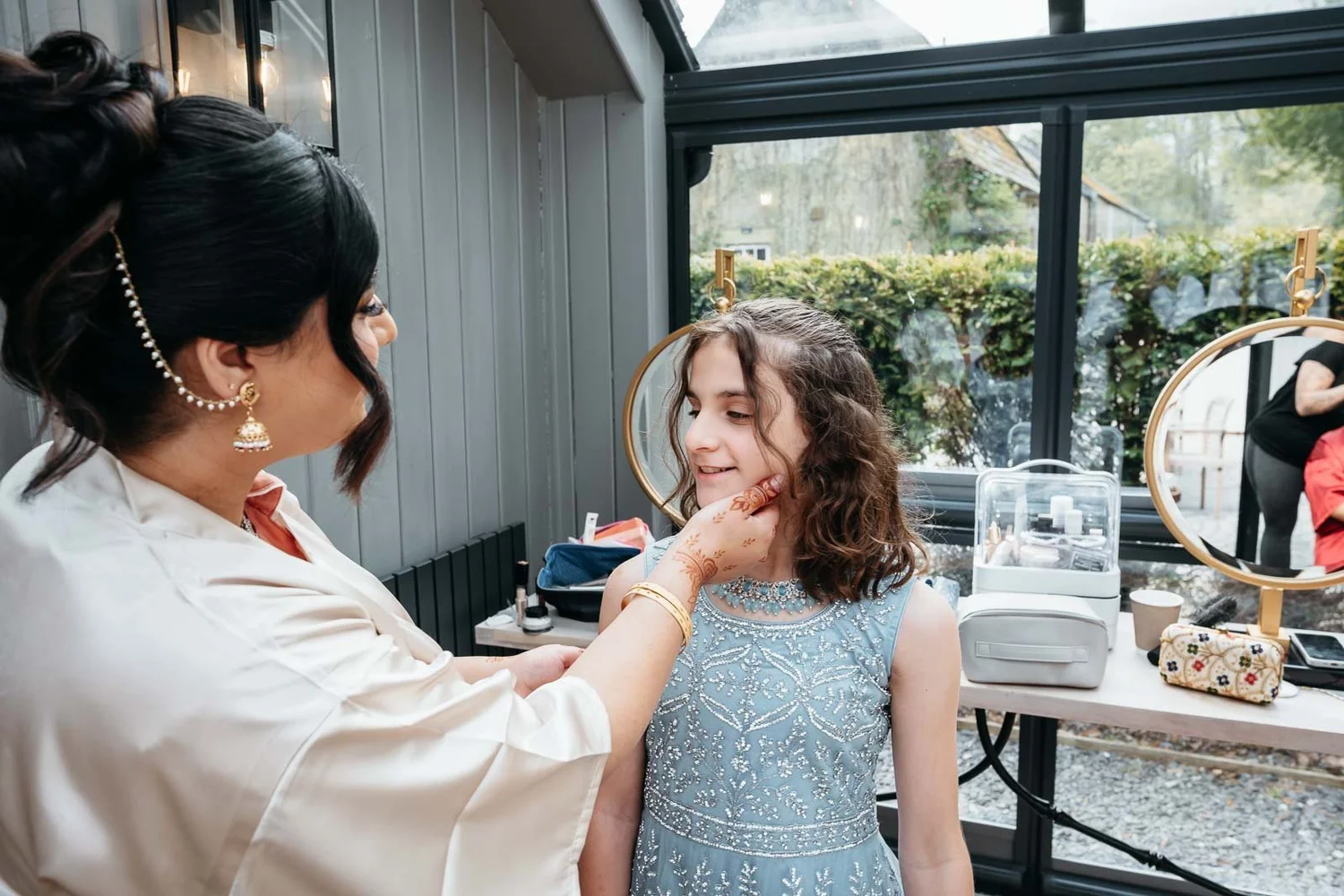 Make-up artist doing a young guest's make-up by a large glass window on the wedding morning at Lartington Hall