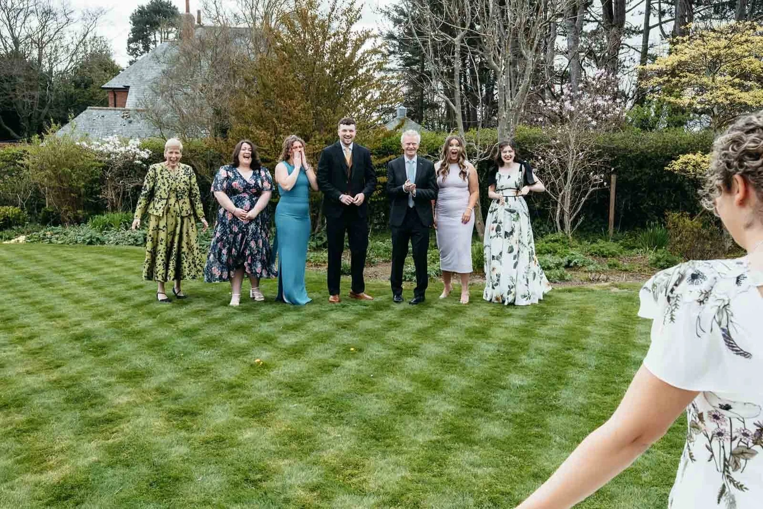 Wedding party on the striped lawn with the gardens behind at Newton Hall, Northumberland