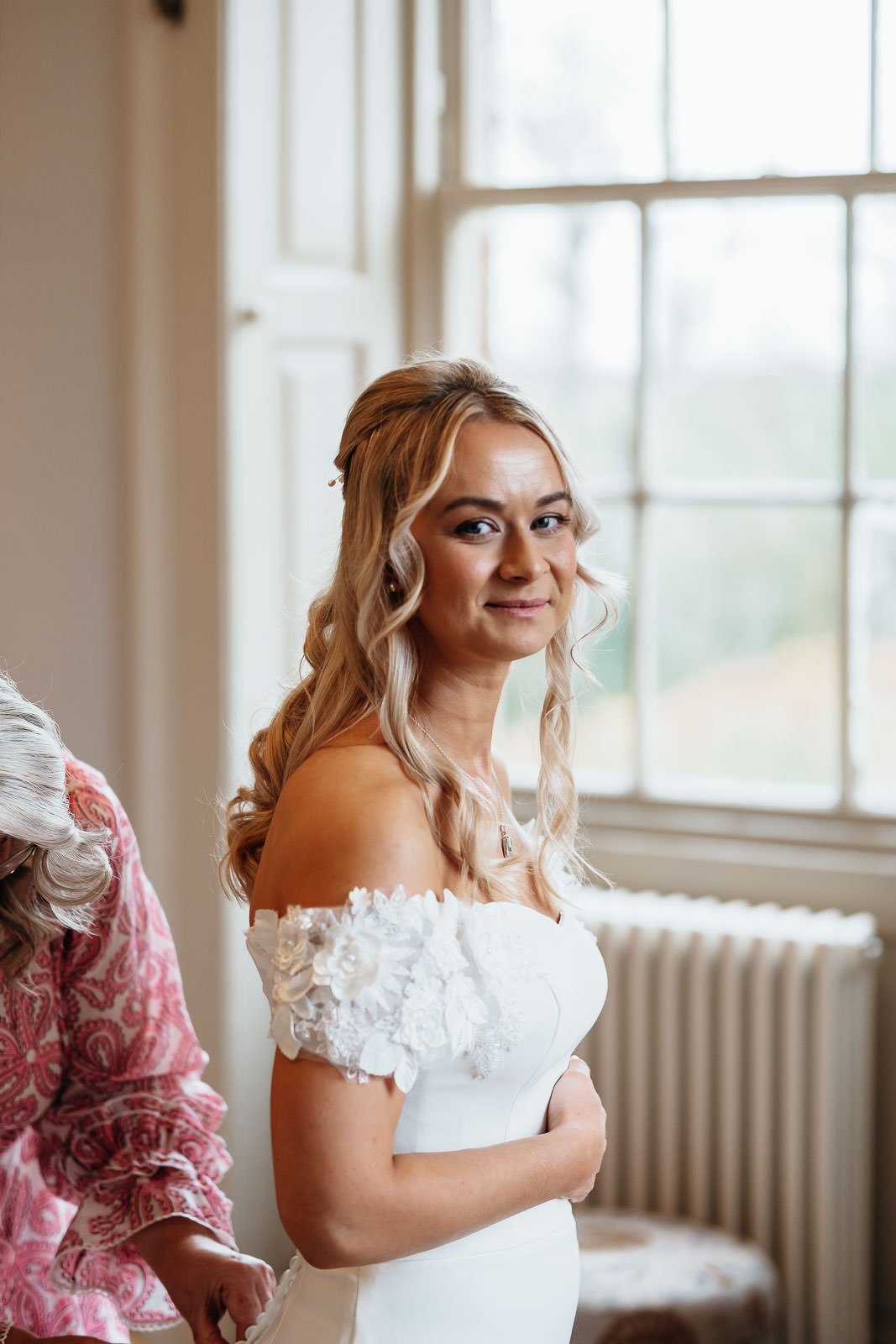 Bride by a sash window in soft light on her wedding morning at Newton Hall
