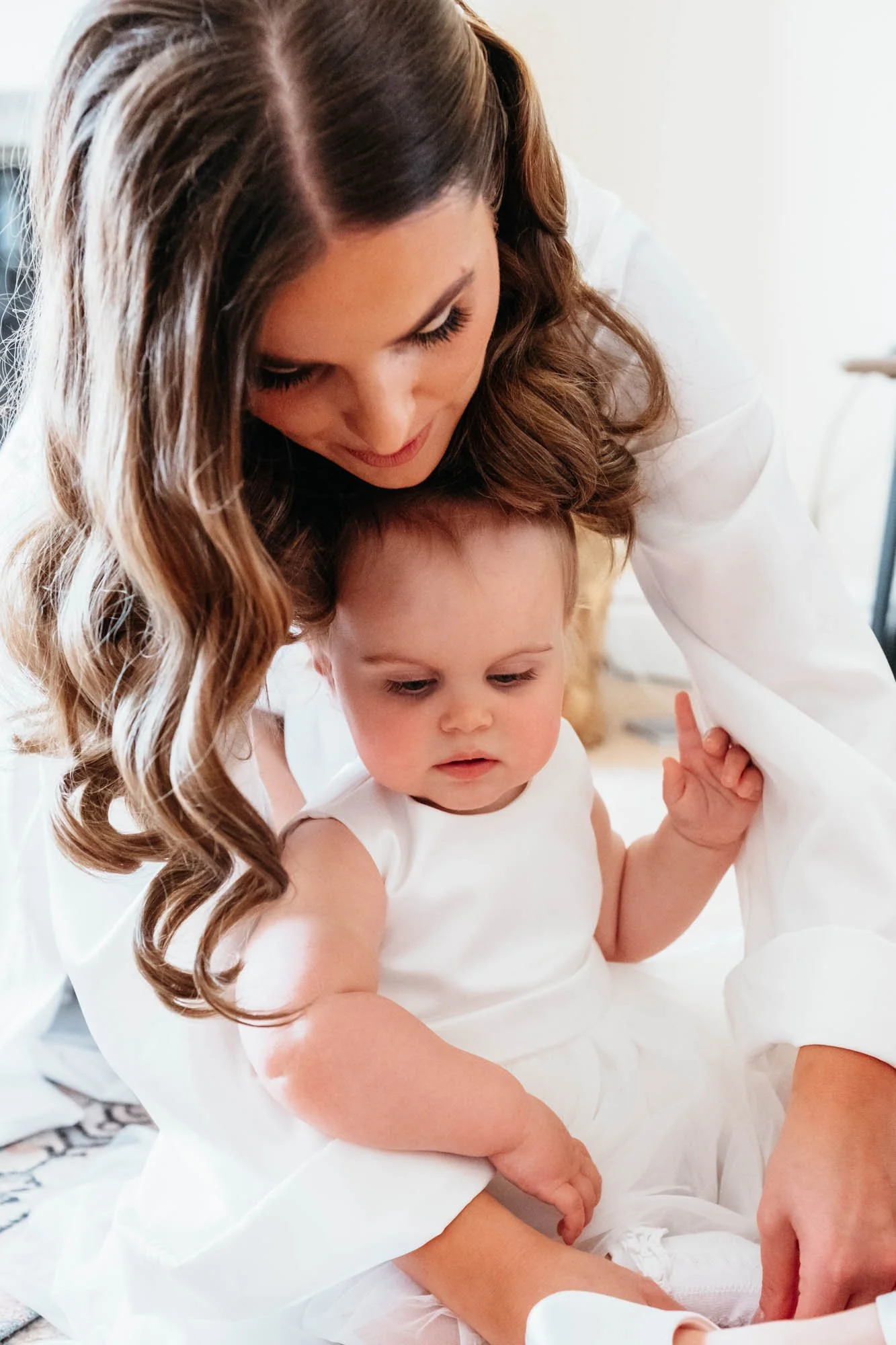 Bride in a white robe holding a baby in a white dress while getting ready at Thirsk Lodge Barns