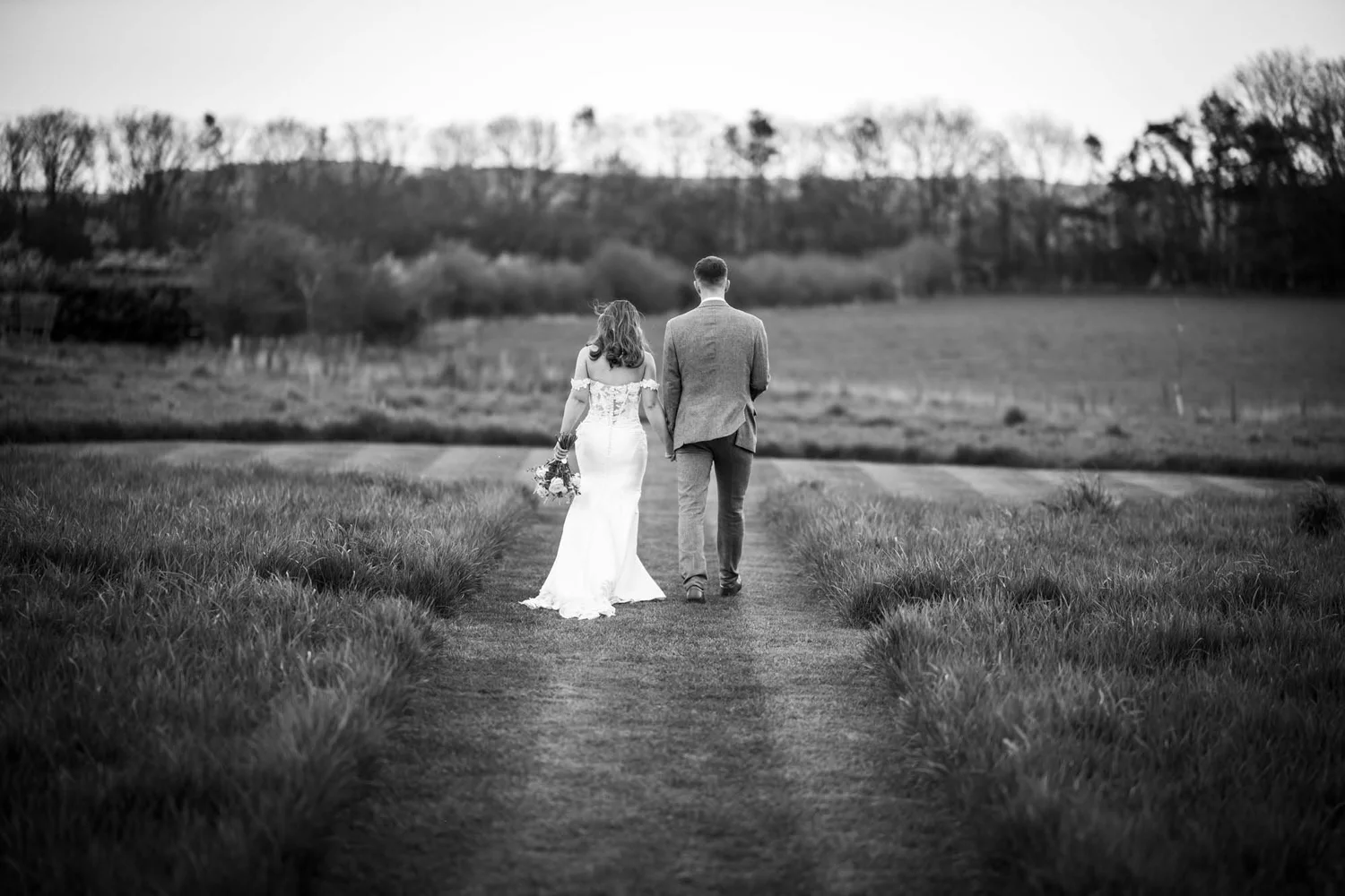 Black and white photo of a couple walking through the meadow at Thirsk Lodge Barns