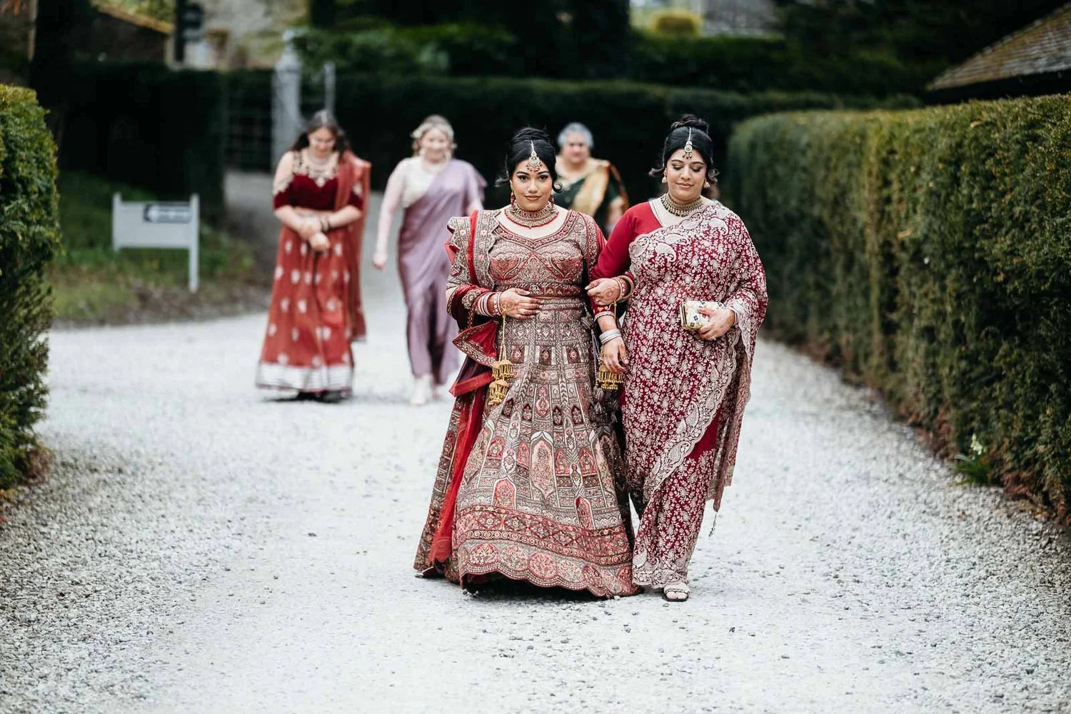 Bride walking up the gravel drive between the hedges with her family at Lartington Hall