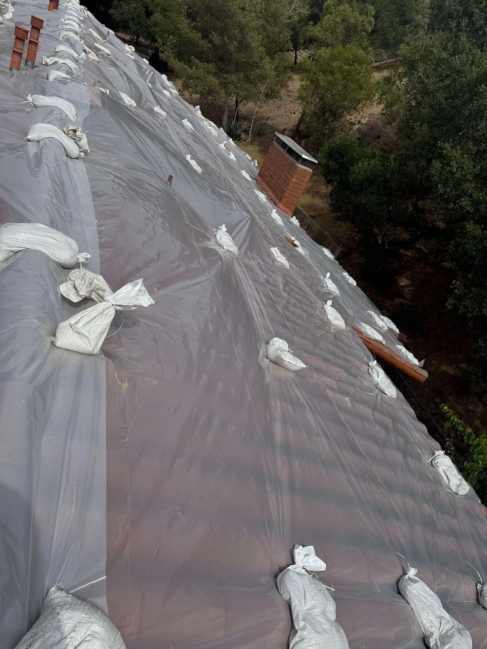 Temporary roof tarp secured with sandbags over a clay tile roof