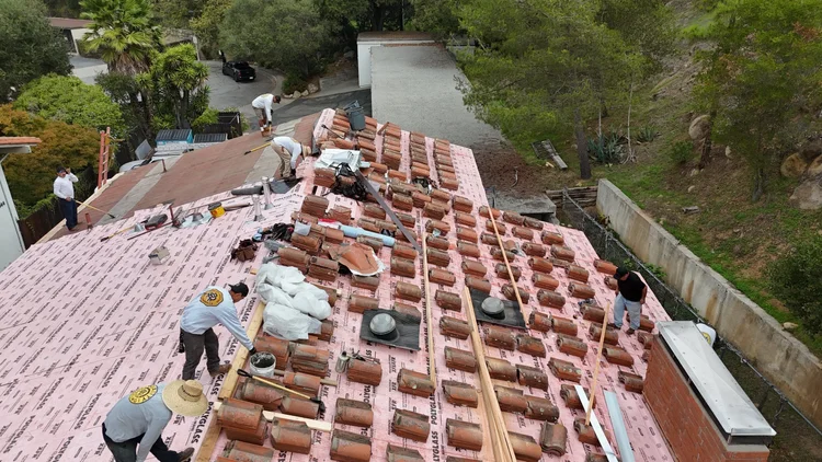 Roofing crew loading clay tile onto new underlayment on a Santa Barbara home