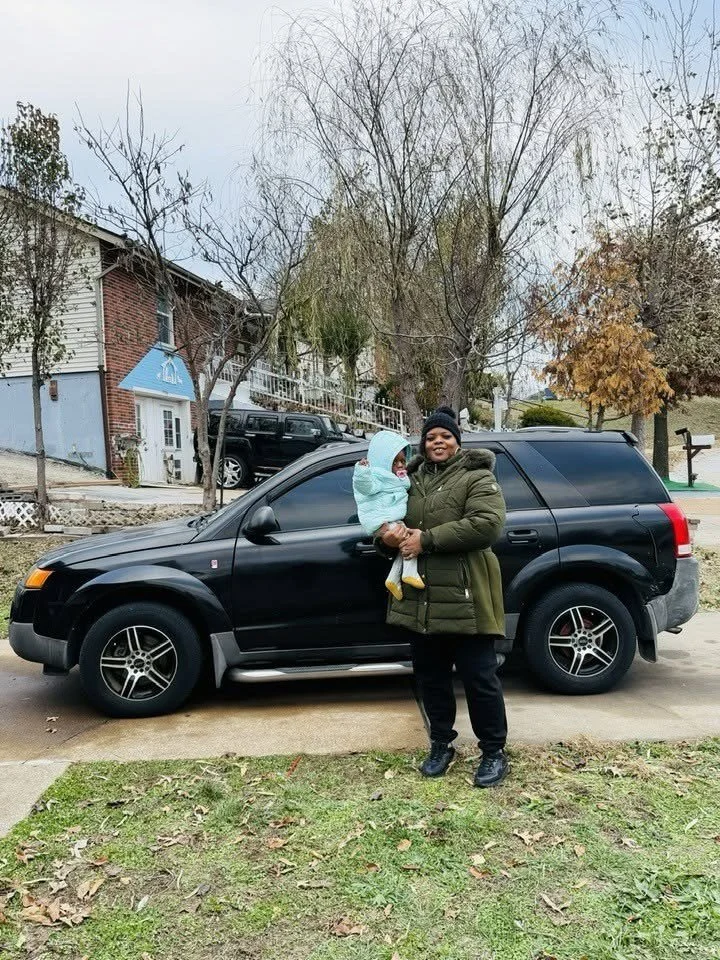 A mom holding her baby beside her new car
