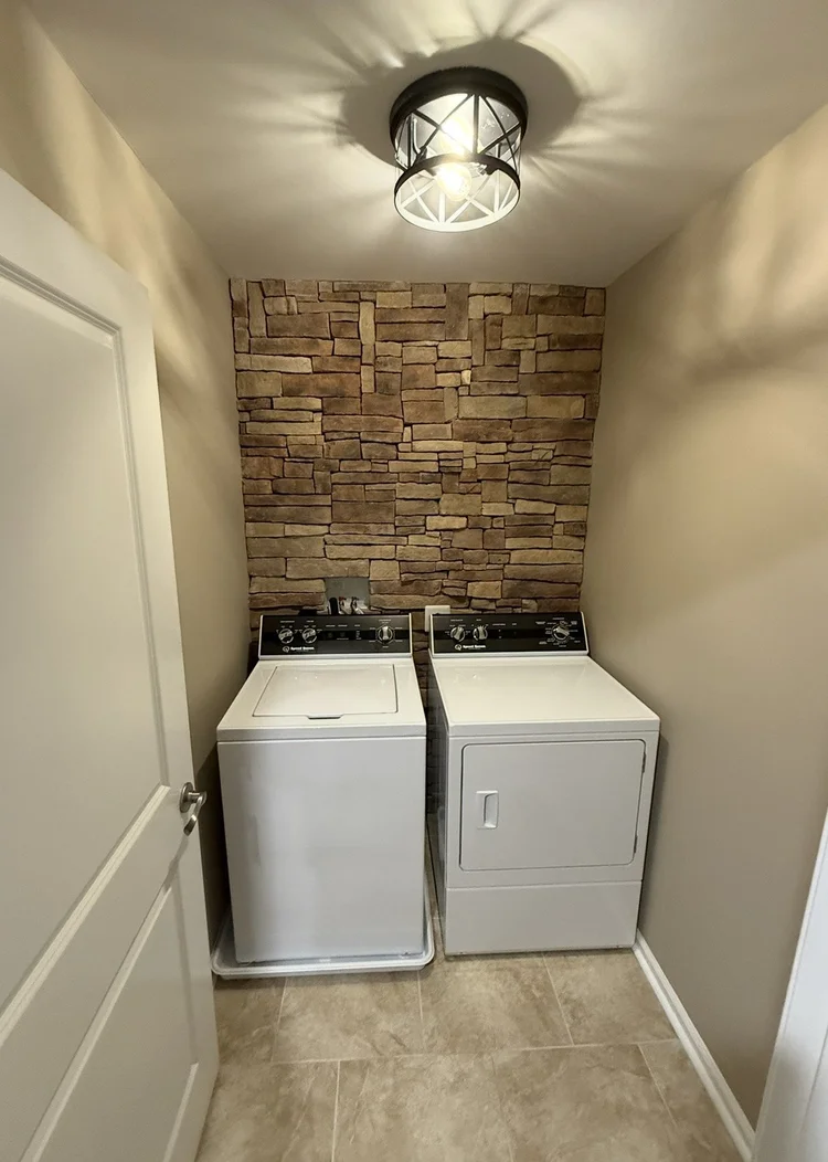 Laundry room with stone-look wall behind washer and dryer