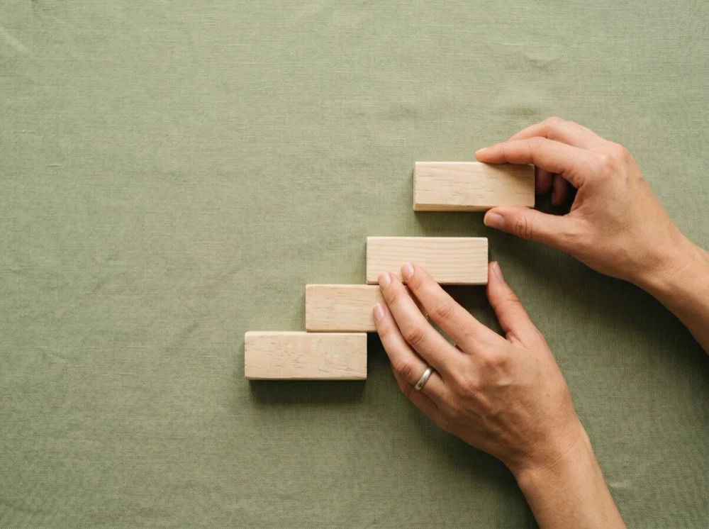 Hands arranging wooden blocks into ascending steps, one at a time