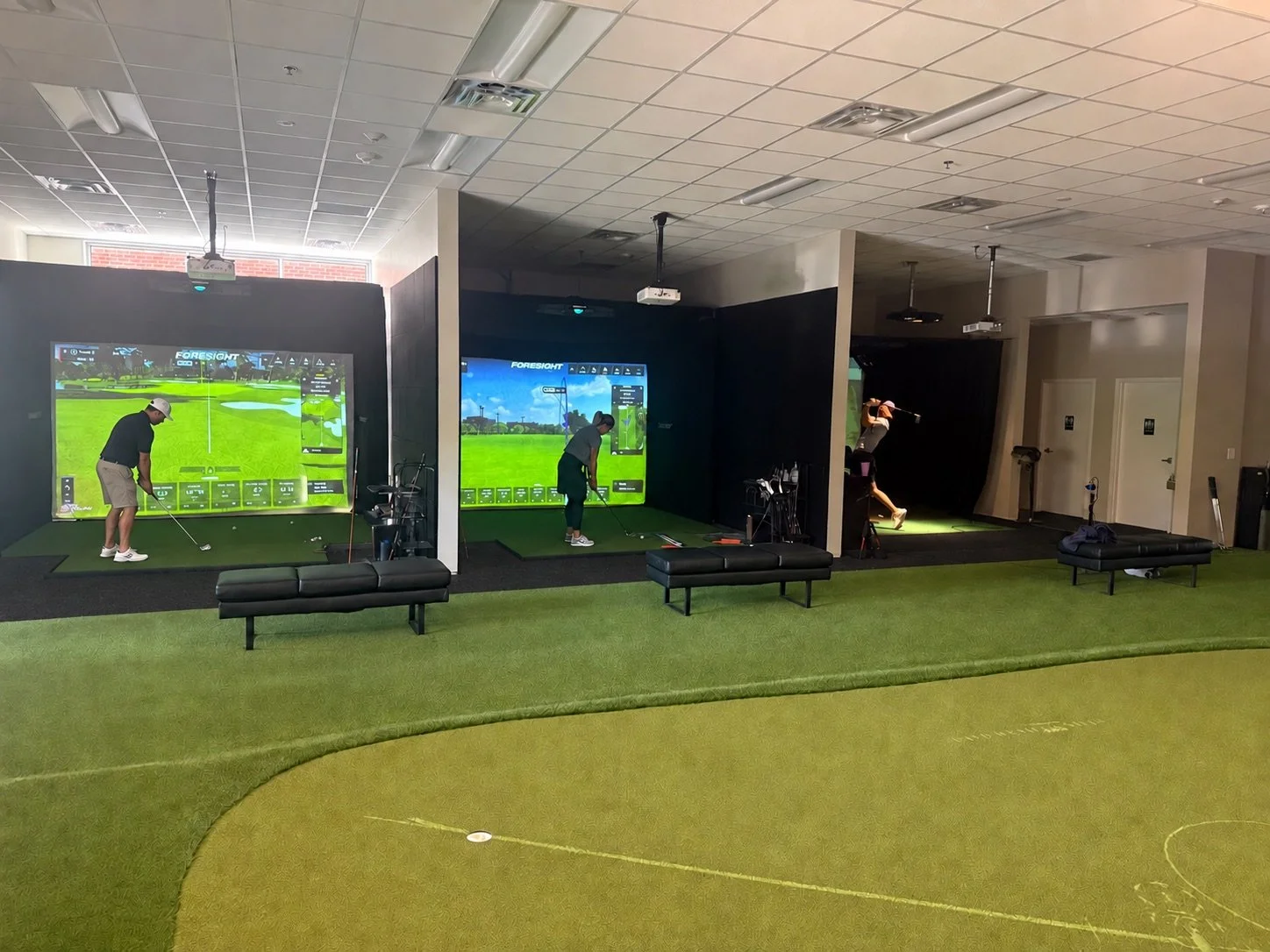 Golfers actively practicing across all three simulator bays at Coastal Golf Academy in Wilmington