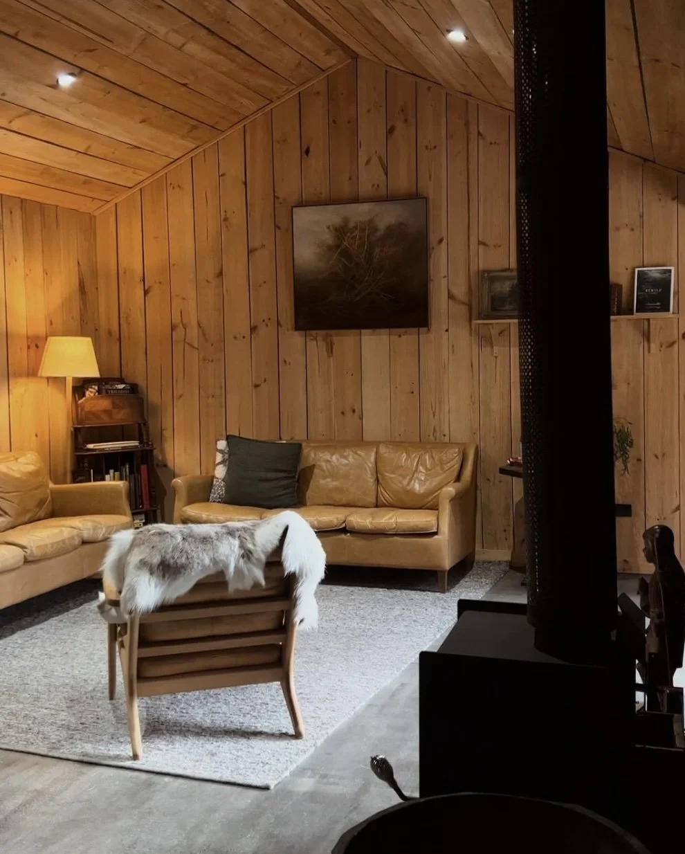 Boscobel Cottage living room — warm pine walls, leather sofas, sheepskin throws and wood-burning fireplace, Southern Highlands NSW