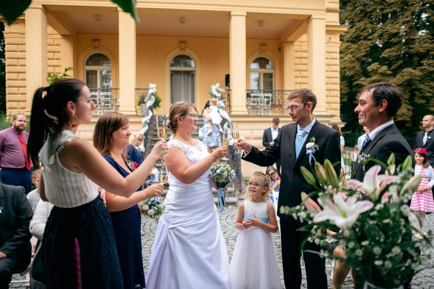 Nevěsta mluví do mikrofonu vedle ženicha a dalšího muže.