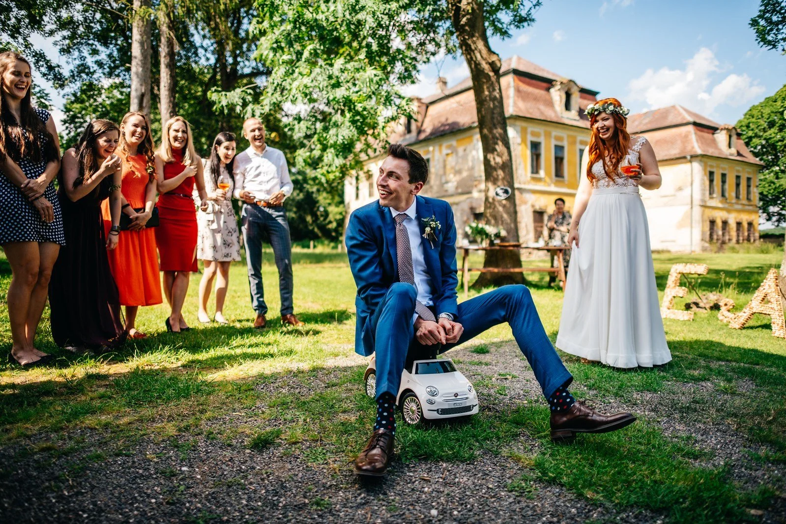 Ženich stojí u zahradní hry, zatímco hosté přihlížejí.