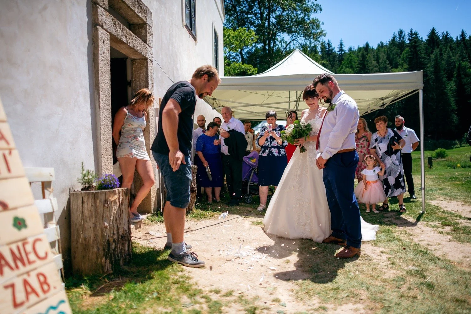Radka s Pavlem se sklánějí k venkovnímu úkolu u špalku, zatímco je sledují hosté.