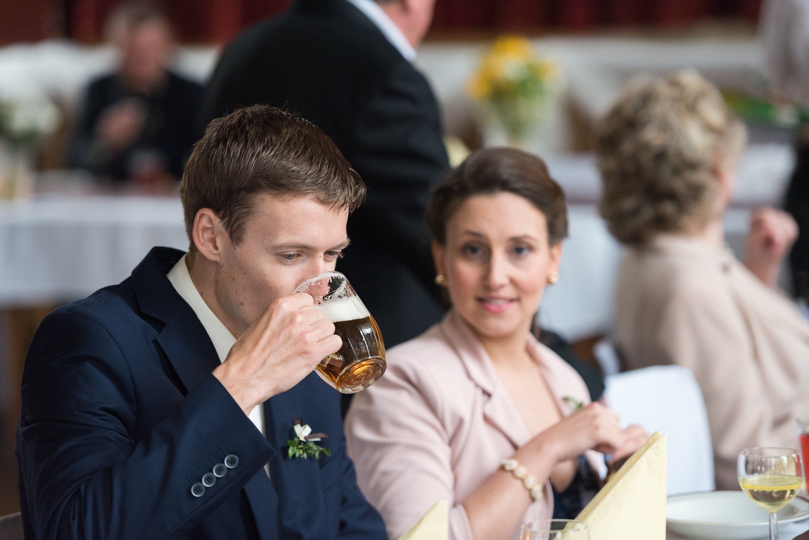 Muž v tmavé košili upíjí pivo u stolu vedle sedící ženy.