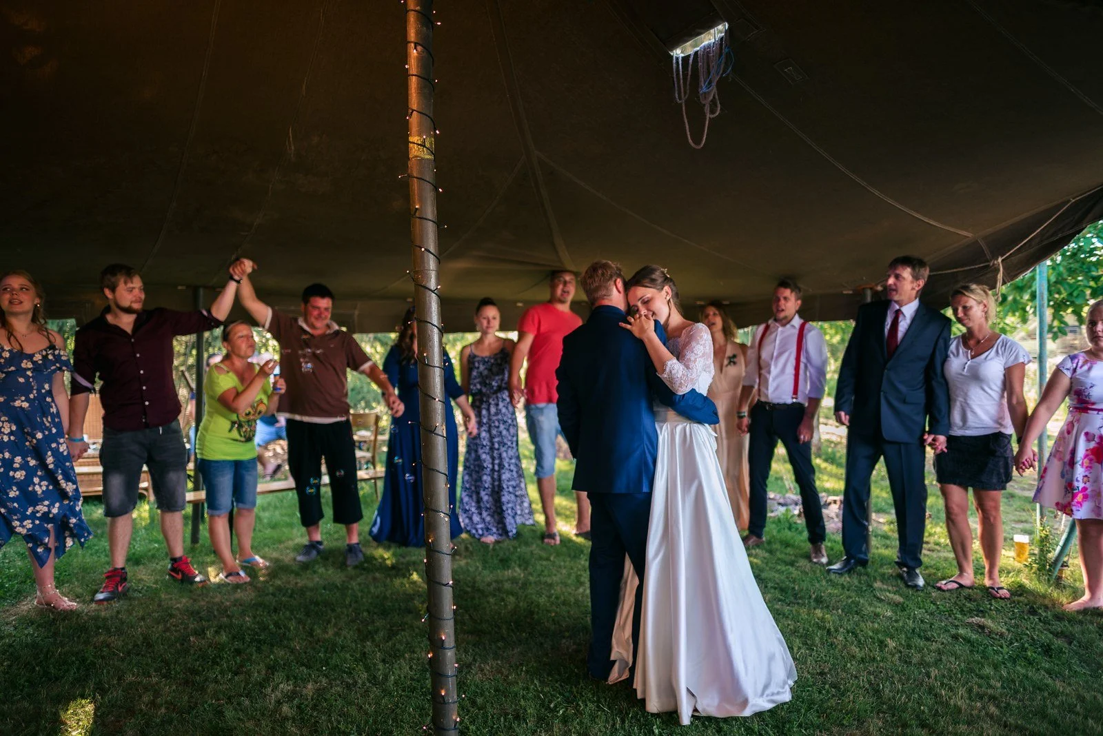 Skupina lidí pod stanem zvedá společně ruce do vzduchu.