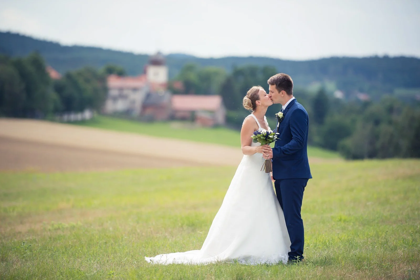 Novomanželé se líbají v otevřené letní krajině.