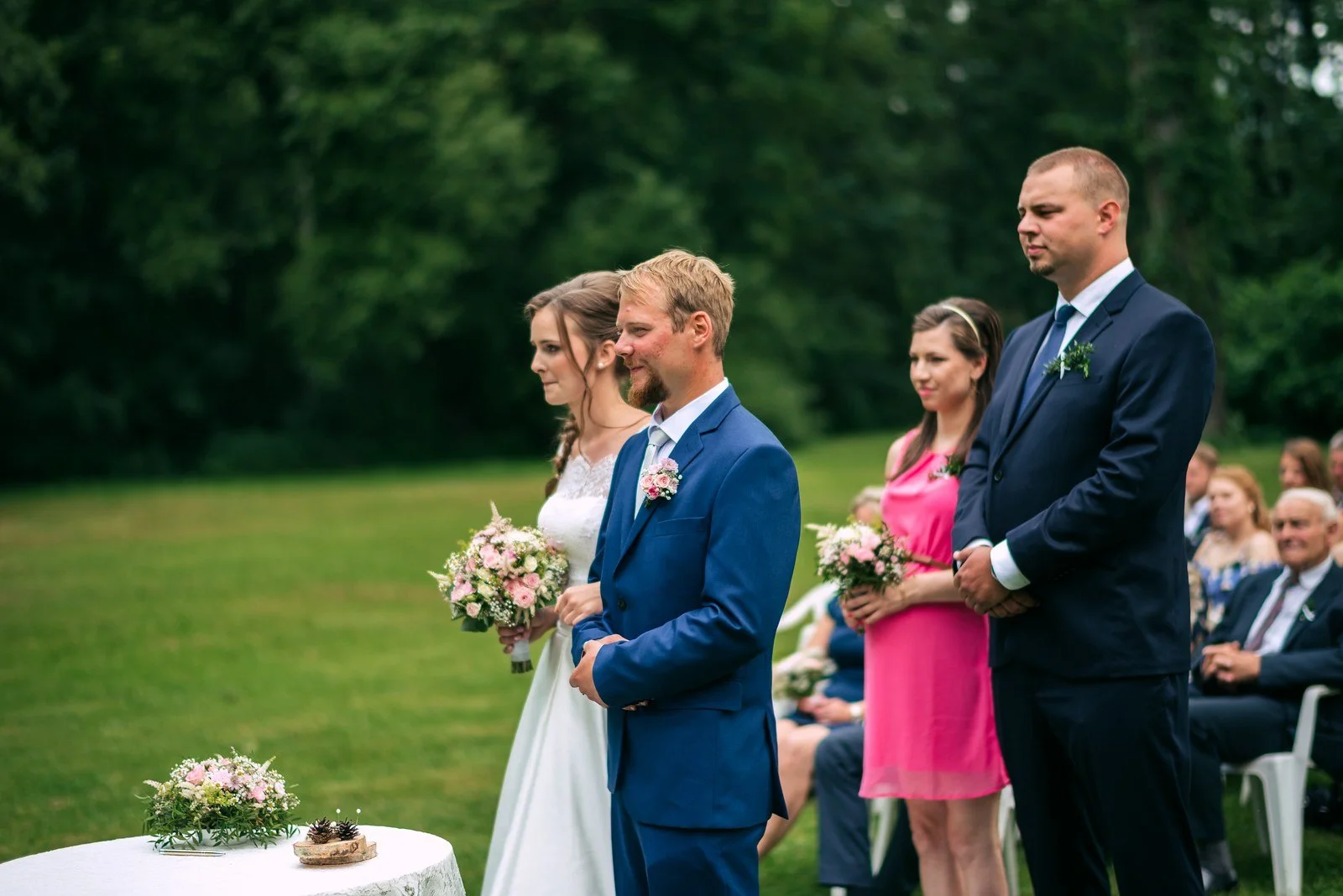Muž v modrém obleku čeká venku před řadami hostů.