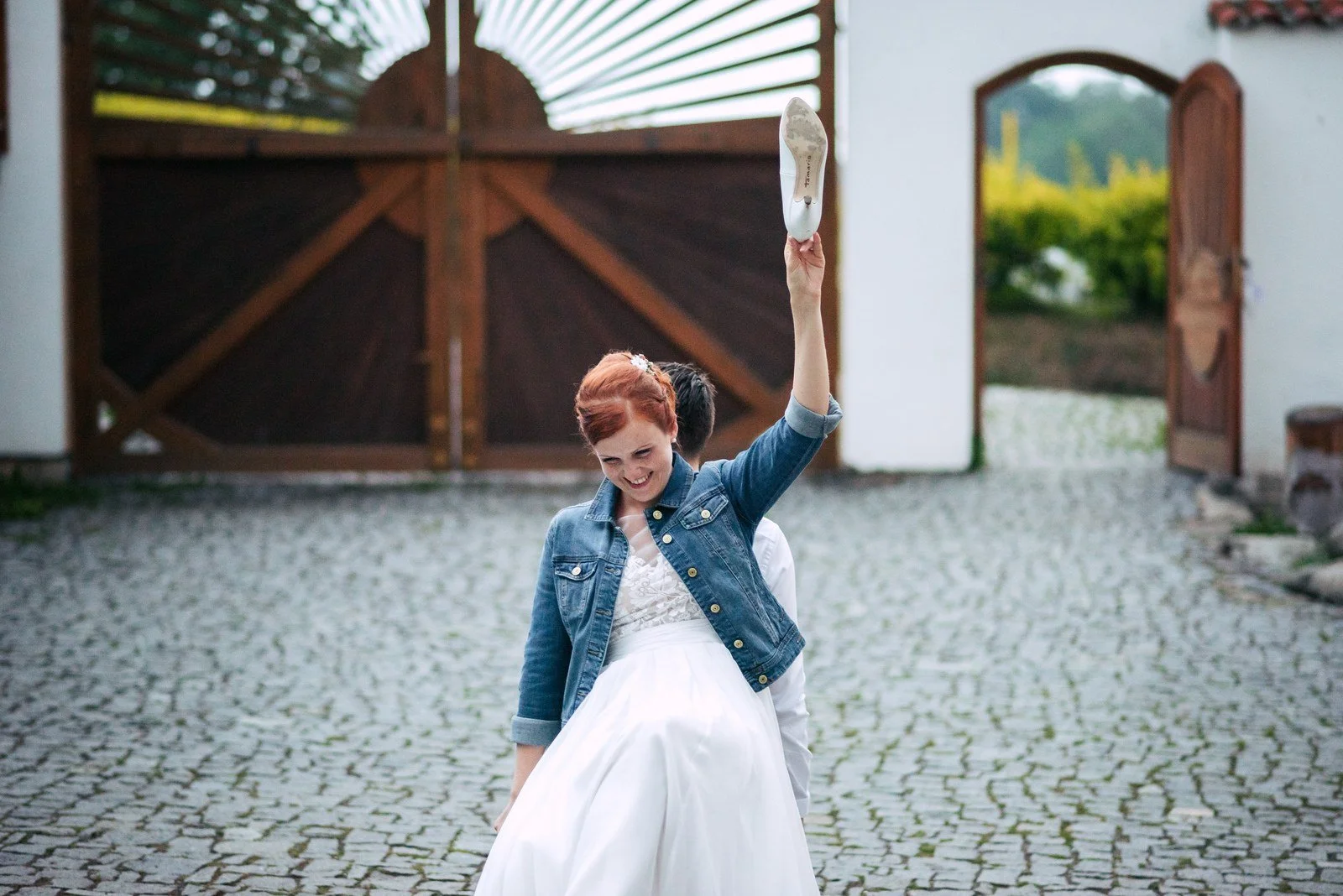 Žena v dlouhých bílých šatech tančí sama na nádvoří s jednou paží zvednutou.