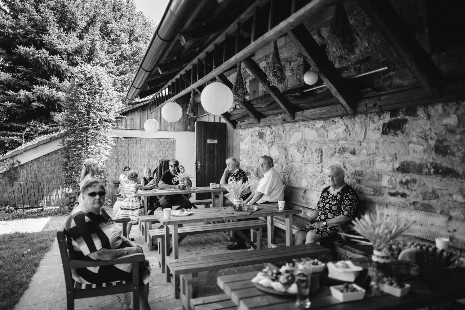 Černobílá momentka hostů sedících pod kamenným přístřeškem