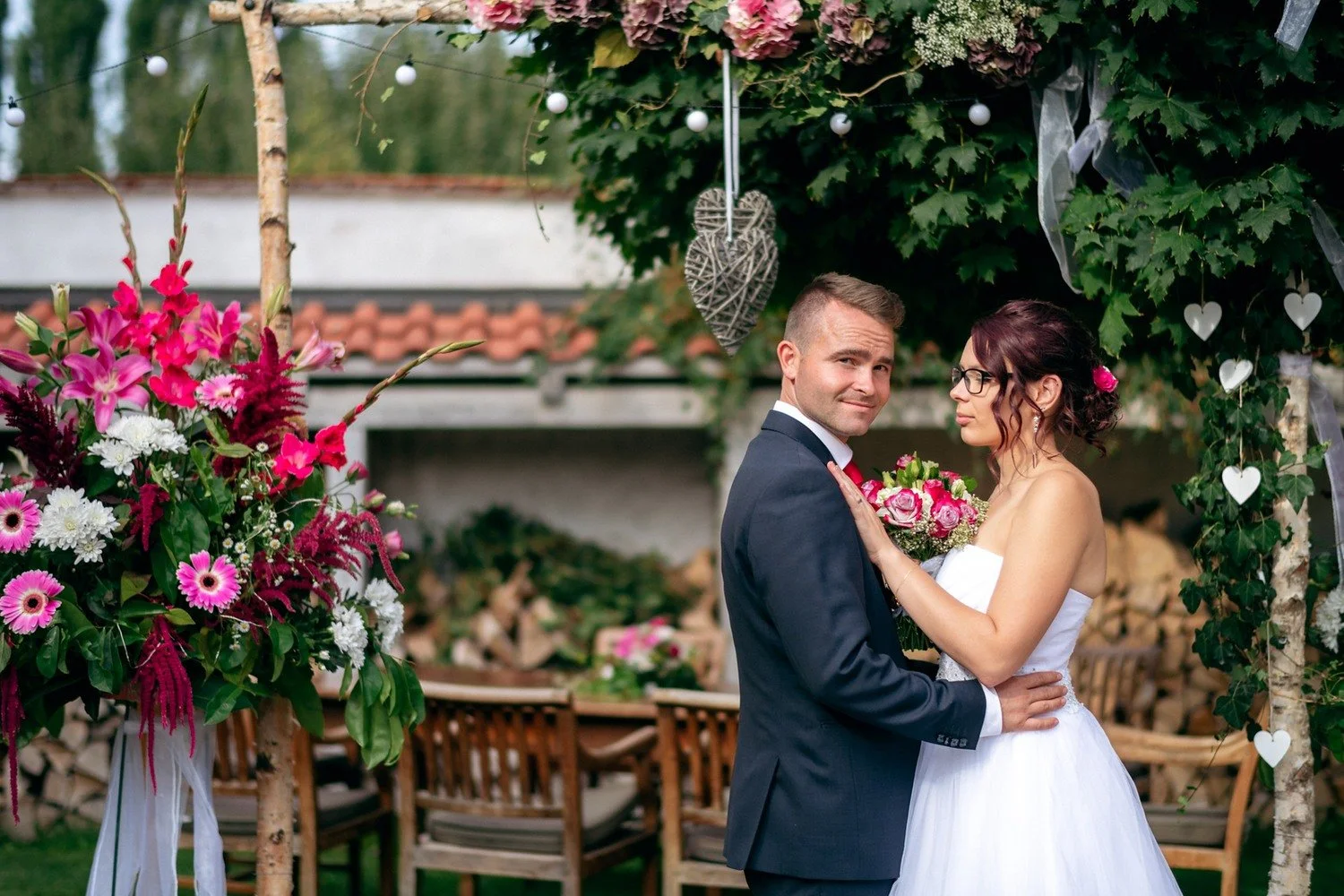 Pár se drží v náručí vedle výrazné růžové květinové výzdoby.