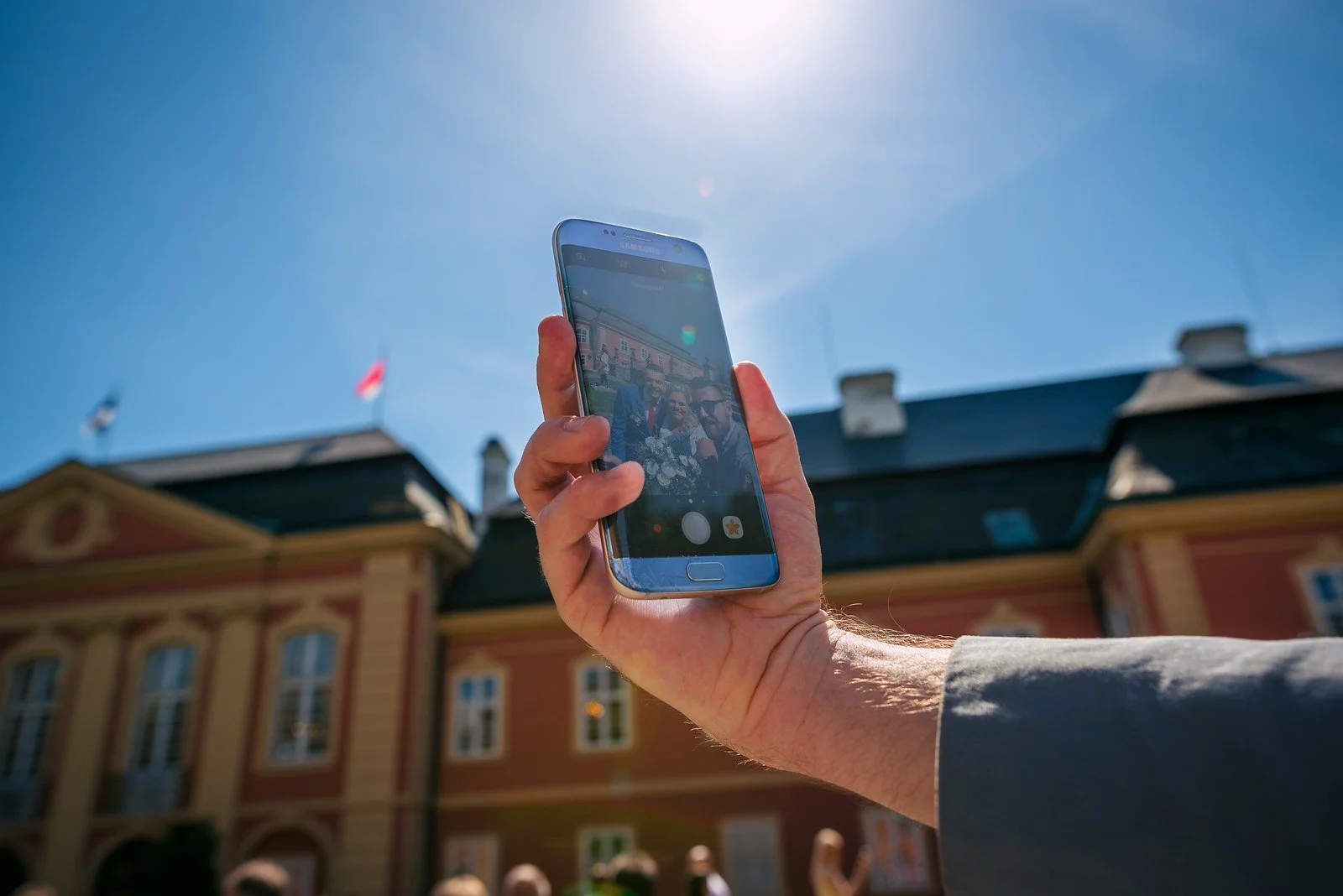 Mobilní telefon fotografuje skupinu před historickou budovou.