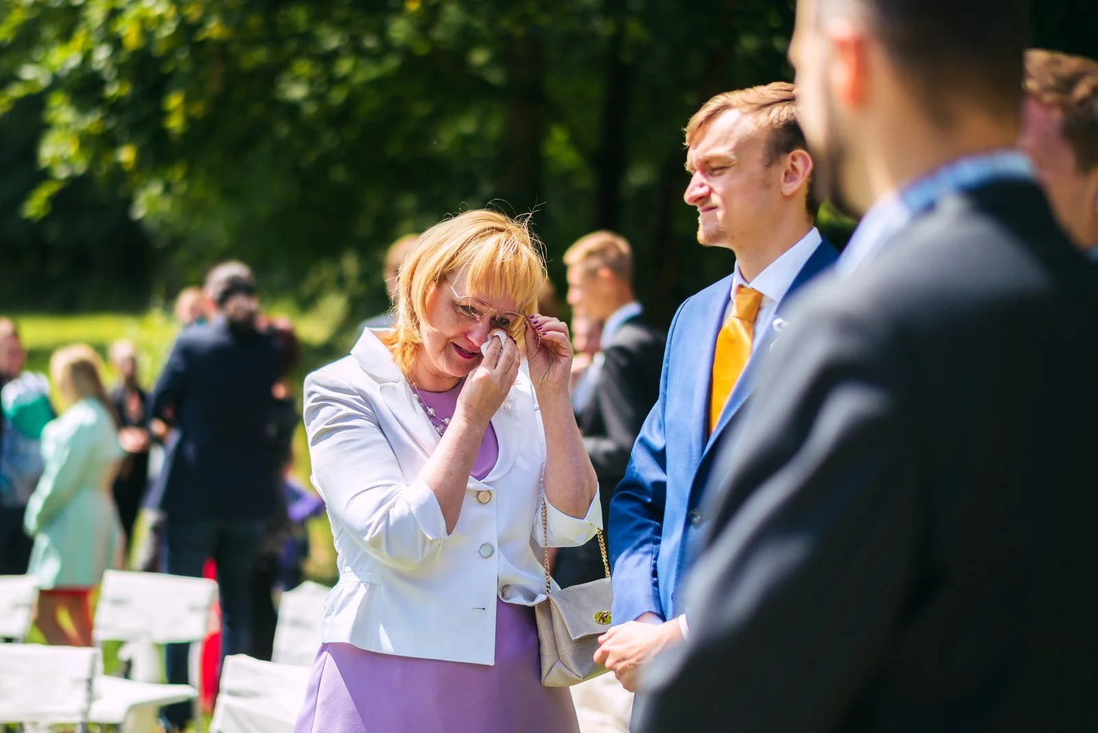Žena navléká prsten muži na ruku před oltářem, mezi nimi je světlá kytice.